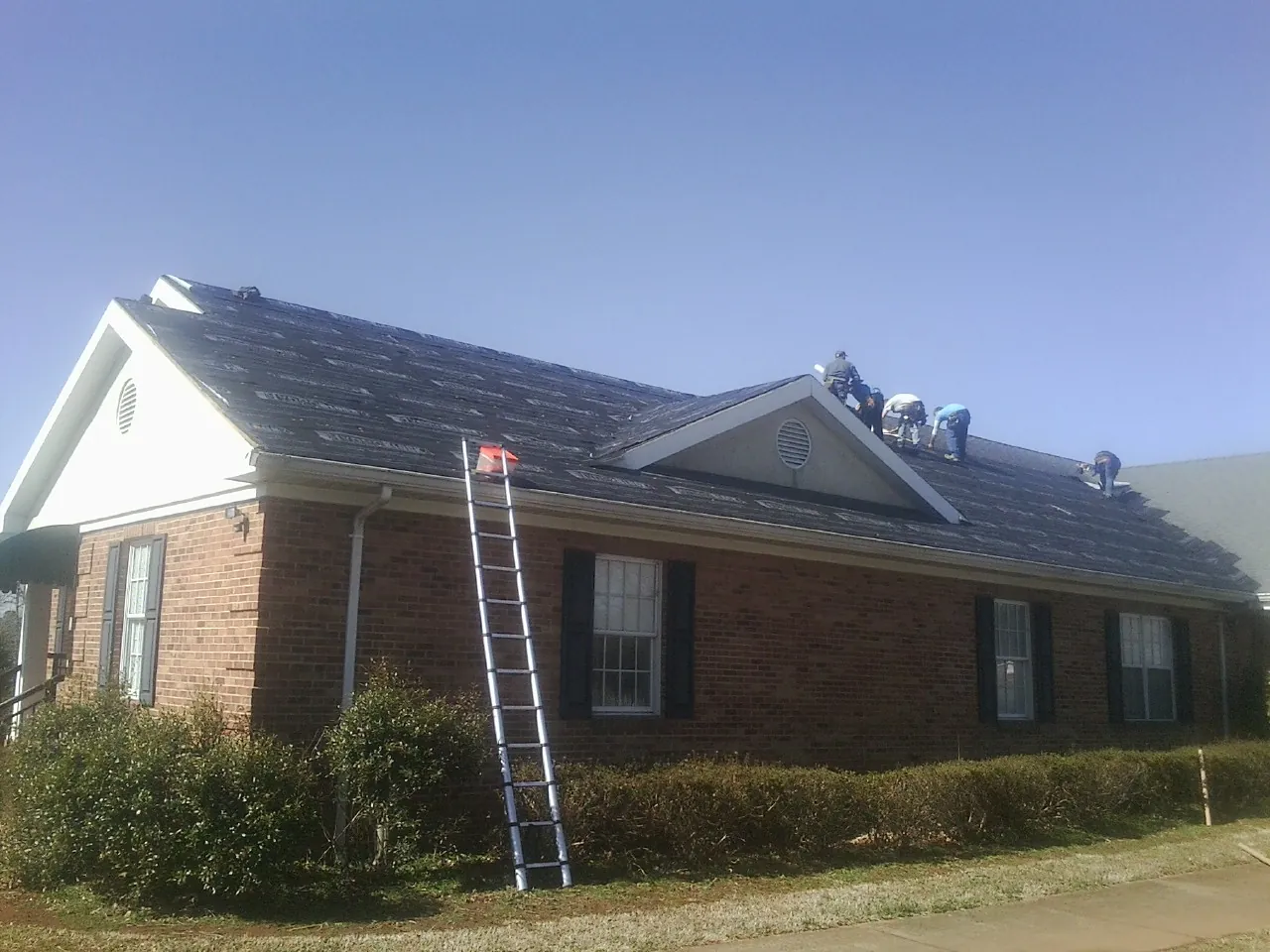 Crew tearing shingles off a brick ranch roof with a ladder set — Emergency Roof Repair work by our crew in Pequannock