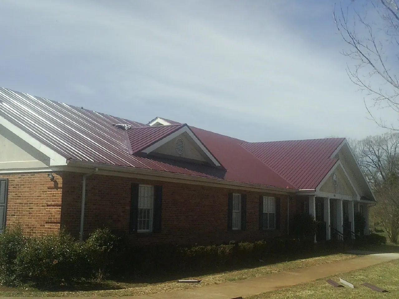 Red metal roof with gabled entries on a long brick building, from a Hail Damage Roof Repair job in Pequannock