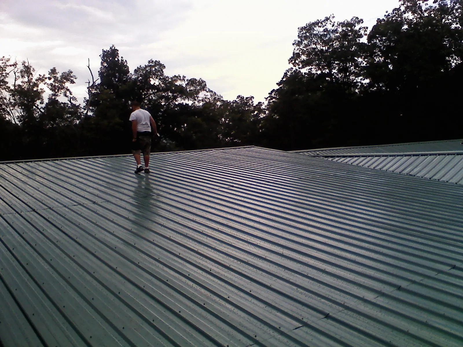 Roofer walking a wide expanse of new green metal roofing in Pequannock