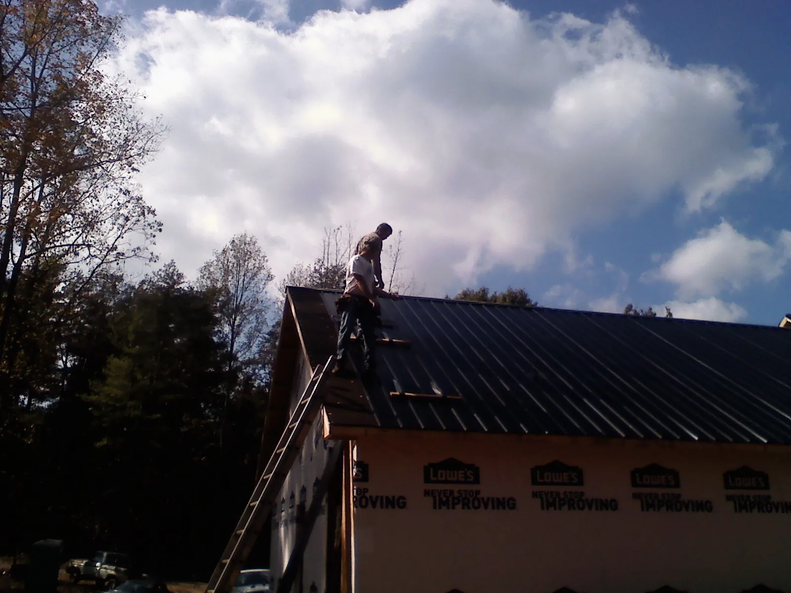 Roofer fastening dark metal panels high against a cloudy sky, from a Roof Inspection job in Pequannock