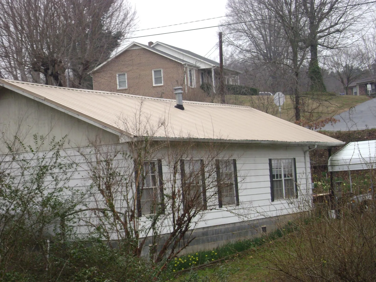 Tan metal roof on a white sided house set into a hillside — Commercial Roofing by Roofing Brothers in Pequannock